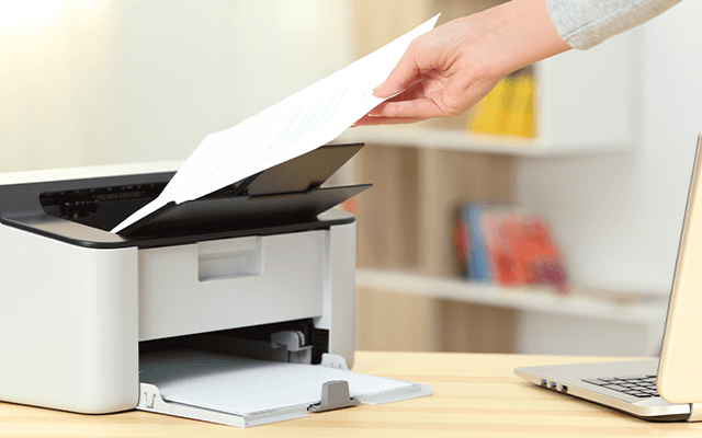 Image of a person holding a piece of paper next to a printer