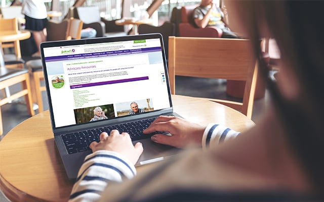 Image of a person sitting at a computer with the Jakafi website on the screen, sitting in a library-like setting